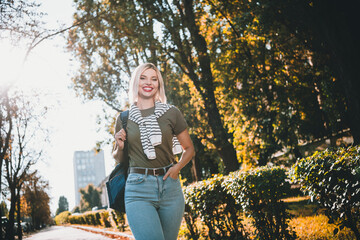 Photo of positive young blonde girl walking wear khaki outfit tied shoulders sweater park sunny...