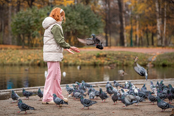 happy red-haired girl feeds pigeons from her hands during a walk in an autumn city park.