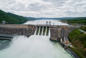 Aerial view of concrete dam releasing water into river on cloudy day. Water discharge at hydroelectric power plant.
