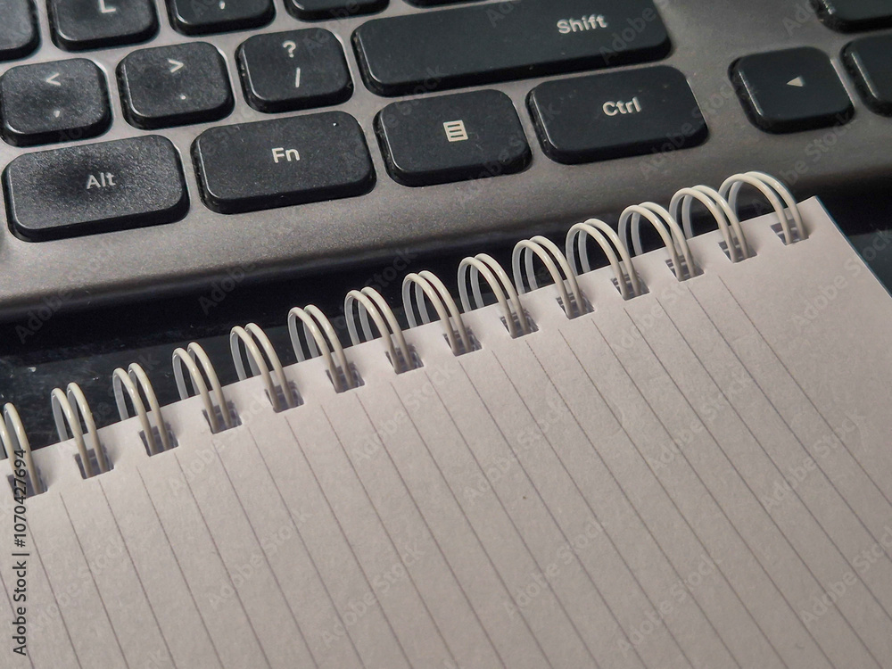 Poster a close-up of a blank notebook lying next to a computer keyboard, ideal for creativity and note-taki