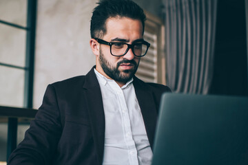 Serious caucasian male lawyer in eyewear vision protection and formal clothes for read information from web page on laptop computer, confident businessman checking mail and analyze data on remote job