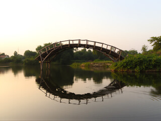 Fototapeta premium A serene bridge arching gracefully over a tranquil pond, surrounded by lush greenery and reflecting calm waters.