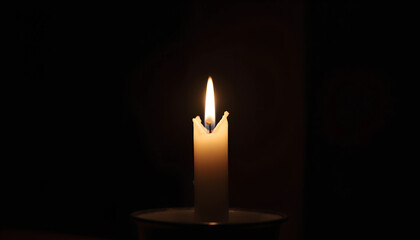 A solitary candle burns softly in a dark room, casting a warm glow during a quiet evening at home