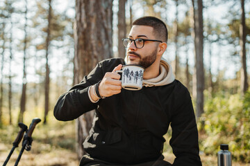 Young caucasian man drinking water taking break from hiking or trekking	
