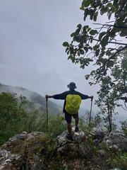 Young traveler and explorer is hiking in the mountains or forest with a backpack in the rainy season and a walking stick.