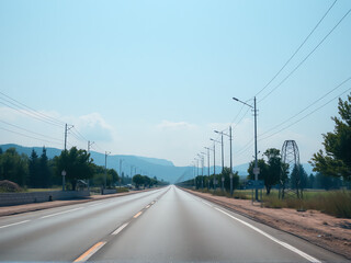 An empty desert road stretches ahead, marked by white lines under a clear blue sky.