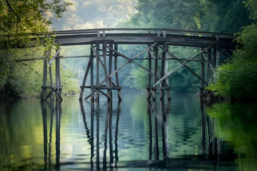 Old wooden bridge over calm river with lush, green surroundings