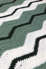 close-up of grandma's retro zigzag striped blanket, in white, dark green and sage green, crocheted or knitted, grandma's house, cozy and warm, diagonal