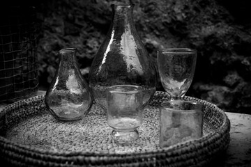 Old glass containers. Collection of retro bottle, amphorae and glasses placed on a wicker tray.