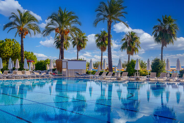 Magnificent view, swimming pool with blue sky with clouds. Holiday hotel in Antalya. Great relaxation and peaceful atmosphere, palm trees, sun loungers reflections.