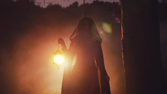 Mystery person, gothic girl ghost queen walking in dark dense fog forest tree hands hold lantern lamp warm candles magic light. long black dress cape. Fantasy woman elf got lost in night wood trees