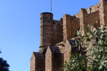 Ancient fortress tower against a clear blue sky with lush greenery in the foreground