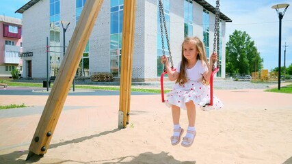 child rides on swing in the park. happy family kid dream concept. child girl swings on a swing at the playground. kid lifestyle playing on swing outdoors