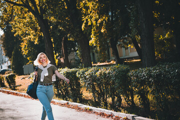 Photo of positive young blonde girl going have fun wear khaki outfit tied shoulders sweater park...