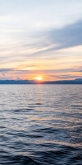Obraz premium Sunset over calm waters with distant mountains on the horizon during early evening