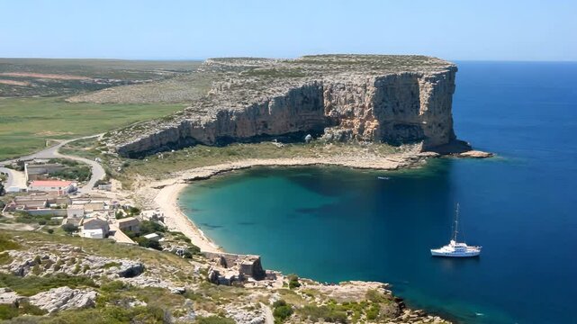 Natural seashore landscape. Cinematic promontory/sea cliff aerial shot. Rural residential area on the coast of an Atlantic ocean. Sailing boat in a turquoise water. Idyllic location for travelling.