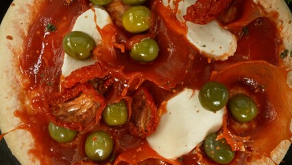 Super slow motion of falling fresh basil leaves on pizza dough with sugo, top down view