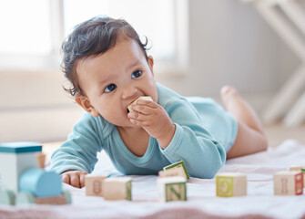Baby, playing and building blocks on floor in home with learning, development and morning in nursery. Child, infant and laying with toys, cube and bite with growth, game and explore in family house