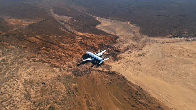 Distant aerial shot of a plane crash in a deserted field. Tragic accident involving aircraft, failed landing, engine failure incident. Damaged debris of an airplane, abandoned ruins. Risks of aviation