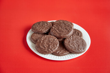 Chocolate cookies with coconut flakes on a white plate against a red background, chocolate cookies on a plate.