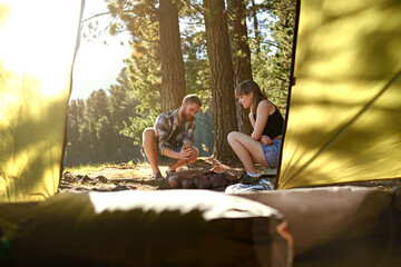 Couple, camping and fire with help outdoor for preparation, heat process and support of vacation. Happy, people and start wood with nature travel, forest safety and trekking bonding for adventure