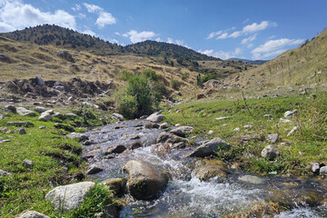 View of landcape with stream in the mountains. Beautiful clouds above mountains and hills. Vivid...