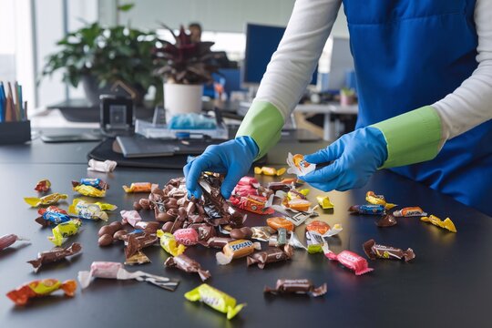 Cleaning Up Candy Wrappers After an Office Party. A worker in protective gloves cleans up candy wrappers left on a desk after an office party. 