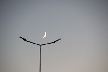 A Beautiful Crescent Moon Hovering Gracefully Above a Streetlight at Dusk, Creating a Dreamy Scene