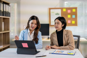 Two businesswomen discussing financial charts and data on a tablet in office meeting