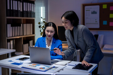 Two young businesswomen working late and discussing over laptop in office at night