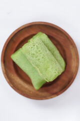 Traditional Indonesian food called 'Dadar Gulung' on a wooden plate, an elliptical cake filled with grated coconut and liquid palm sugar, Dadar gulung top view isolated on a white background.