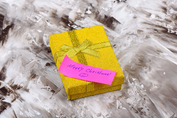 Yellow gift box with handwritten note Merry Christmas on abstract surface.