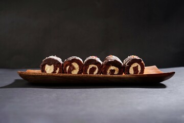 Chocolate roll cake with fresh cream in wooden plate isolated on dark background. chocolate swiss roll cake.