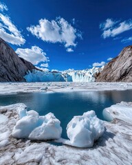 Obraz premium A breathtaking view of a glacier with ice formations and a tranquil blue lake under a clear sky filled with fluffy clouds.