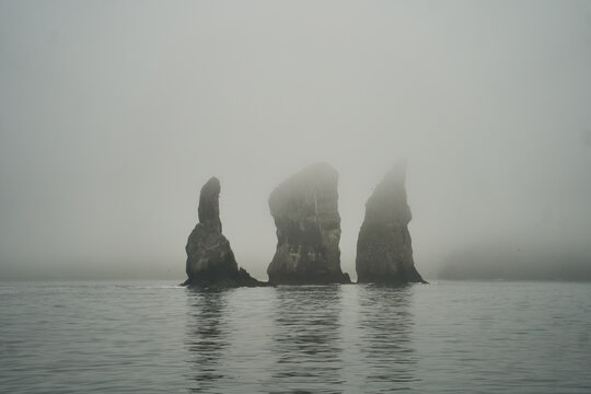 Try Brata, Kamchatka. An eerie mist gently surrounds the towering rock formations that majestically rise from the calm, serene waters