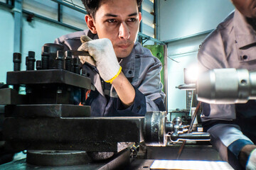 Two focused industrial technicians work together operating heavy machinery in a workshop. The image of teamwork, precision, and technical expertise in an engineering and manufacturing industry