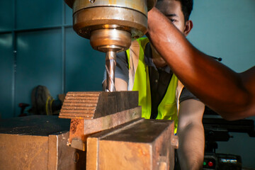 An industrial worker operating a drill press in a workshop. The focus is on the precision and concentration required to handle machinery. The worker wears a safety vest, ensuring a secure work.