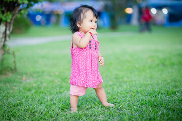 Baby girl walking outdoors dressed in pink stripped dress. Happy kid. Happy childhood.