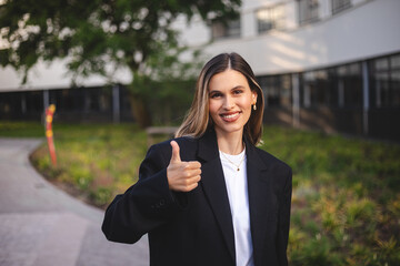 Portrait of confident blonde business woman in shirt and jacket showing thumb up in approval,...