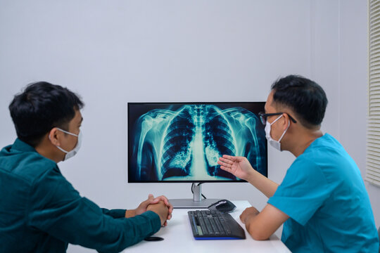 Asian male doctor explaining chest x-ray on computer screen to patient who came to hospital and encouraging patient after receiving chest x-ray result