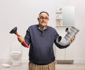 Confused mature man holding a pipe and a toilet plunger