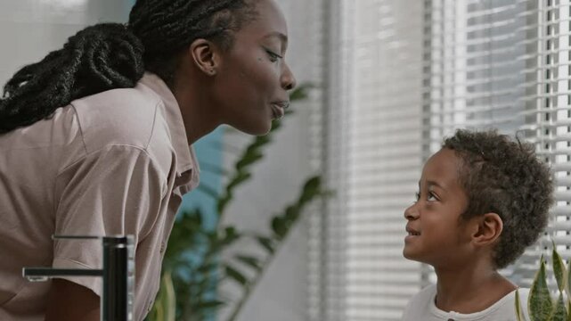 Smiling young Black woman with braided hair receiving gentle face massage done by her little son with use of quartz roller