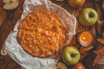 Top view of a freshly baked apple pie surrounded by fresh apples, wooden spoons, a lit candle, and...
