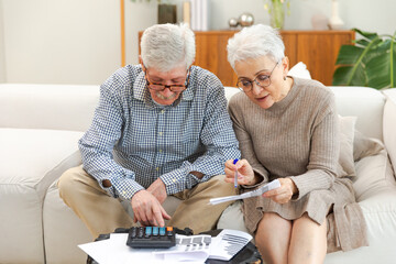 Middle aged senior couple sit with laptop and paper document. Older mature man woman reading paper...