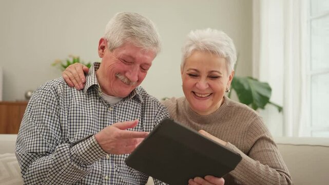 Senior old couple with tablet watching video online. Husband wife spending time together at home. Happy modern mature senior couple using tablet for family entertainment. Old people modern technology