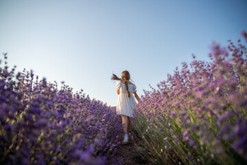 Lavender field girl. Back view happy girl in white dress with a scythe runs through a lilac field of lavender. Aromatherapy travel