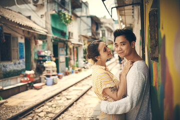 Fototapeta premium City, railway and couple in portrait for hug, travel adventure or explore vacation for anniversary. Interracial marriage, woman and man with romance for admiration, love or bonding outdoor in Vietnam
