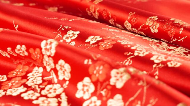 Lustrous red silk textile fabric background with floral golden embroidery in oriental style with plum blossom flower pattern. Soft folds of brocade shimmers beautifully on a rotating display case. 