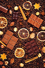 Background of coffee beans, dark and milk chocolate pieces, cinnamon, dried orange and star anise.