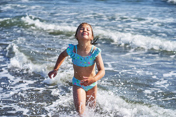 Fototapeta premium An 8 year old girl in a swimsuit having fun in the sea waves.